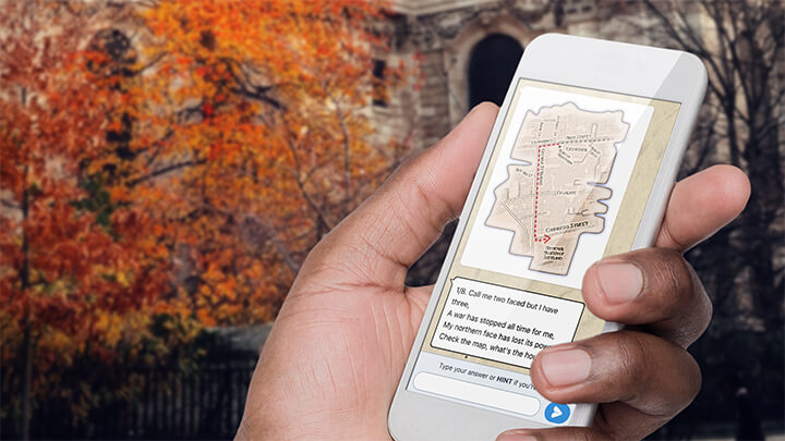 A hand holding a phone playing Treasure Hunt Bristol with a tree with orange leaves behind.