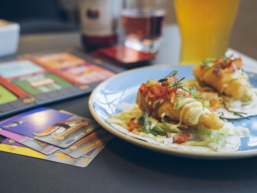 Delicious food and beer next to cards from a board game