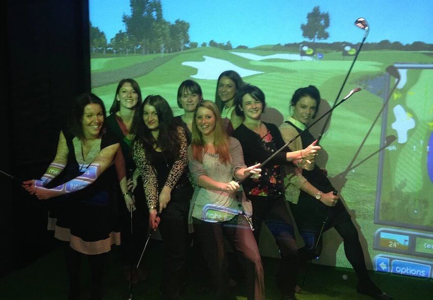 A group of girls holding golf clubs in front of a golf simulator screen